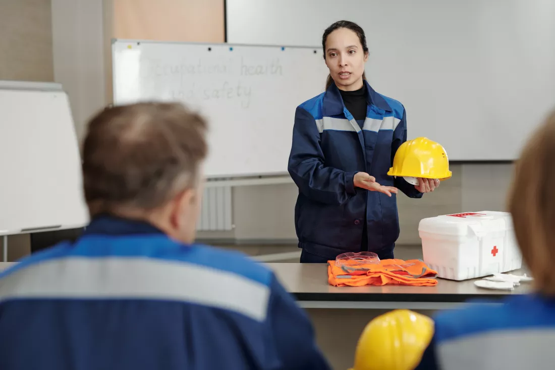 young-serious-female-holding-protective-helmet-while-standing-by-desk-front-colleagues-describing-it-basics-life-safety-lesson